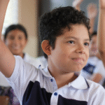 Niño participando en clase, levantando la mano con entusiasmo durante una actividad educativa. Representa la diversidad de estilos de aprendizaje en el aula.