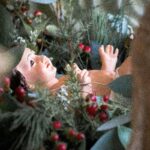 Figura del Niño Jesús recostada en un pesebre de hojas y bayas rojas, símbolo de la Natividad.